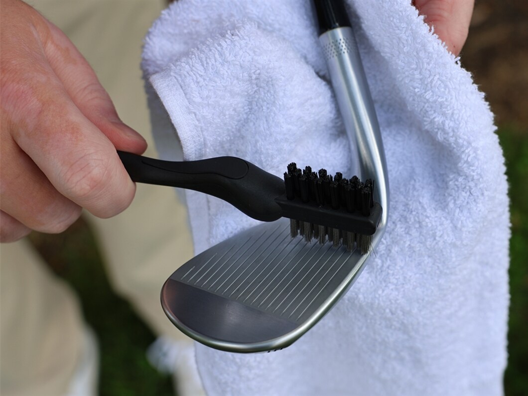 Person cleaning the golf club grooves on a wedge with a towel
