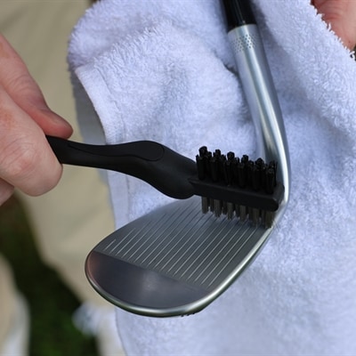 Person cleaning the golf club grooves on a wedge with a towel