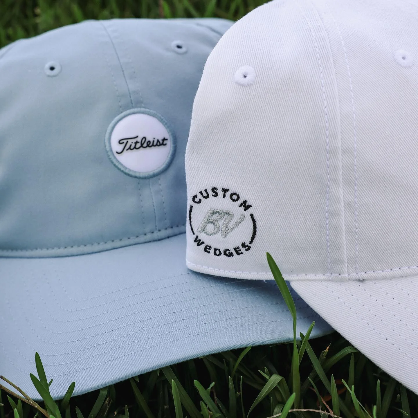 Two Vokey Design headwear caps, one light blue and one white, with the Titleist brand logo.