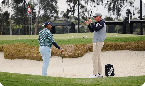 Two golfers standing in a golf course bunker.